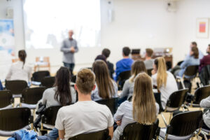 Image of students watching a person lecture in a classroom.
